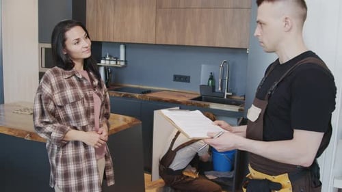 Plumber Repairs Sink as Customer Signs Clipboard