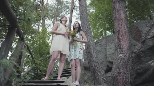 Two Women Friends Holding Flowers in the Forest