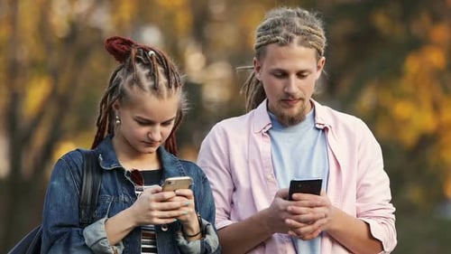 Young Man and Woman Using Mobile Phones Outdoors