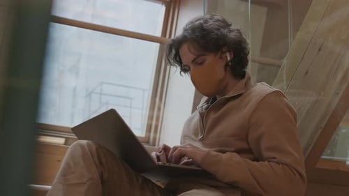 Young Adult Using Laptop on Stairs with Face Mask