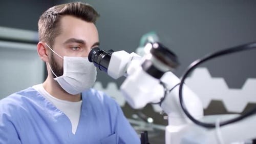 Male Dentist in Face Mask Using Dental Microscope