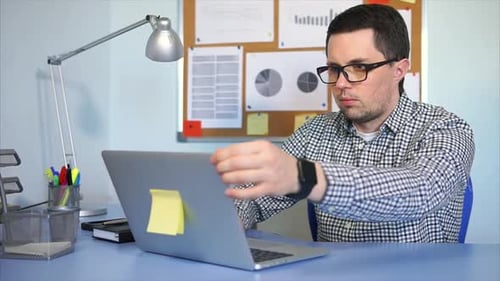 Businessman Sitting at Desk in Office, Working on Laptop Computer.
