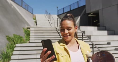 Woman with Skateboard Using Smartphone Outdoors