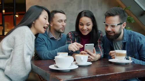 Joyful Youth Men and Women Talking and Laughing Looking at Smartphone Screen in Cafe