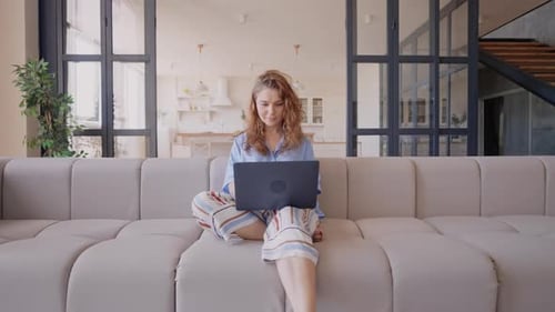 Smiling Woman Uses Laptop on Couch at Home