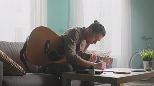 Musician Plays Guitar and Writes Song at Home