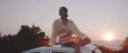 Woman Sits on Car at Sunset