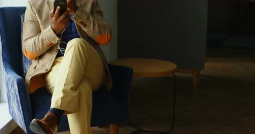 Senior Man Sits in Chair and Uses Phone