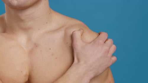 Man Massaging Bare Shoulder Against Blue Backdrop