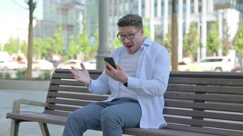Man Sitting on Bench Using Smartphone in City