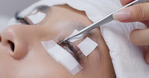 Colagem de cílios artificiais com pinça no olho da mulher, extensão dos cílios
