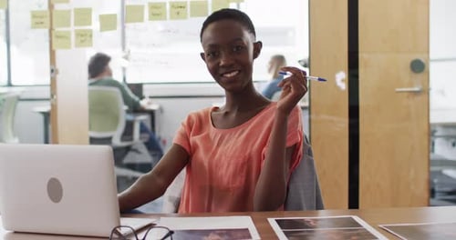 Portrait of african american businesswoman sitting at desk with laptop and smiling in office