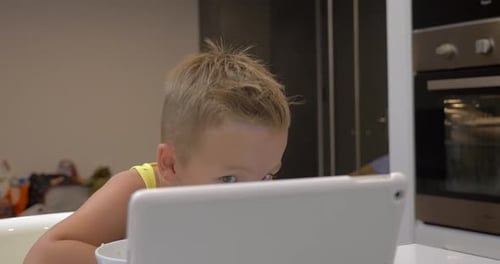 Blond Boy Eats Breakfast While Watching Tablet