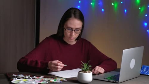 Woman Drawing in Notebook at Desk with Laptop