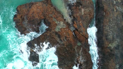 Aerial View of Waves Break on Dark Rocks Near Beach. Ocean Waves Crashing Against Rocky Shore