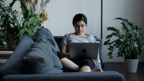 Woman at Home Sitting on a Couch Works on a Laptop Computer. Girl Using Computer