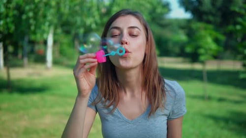 Young Woman Blowing Bubbles in a Green Park