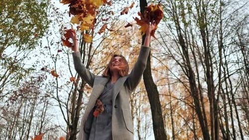 A Young Girl Throws Up Leaves in an Autumn Park