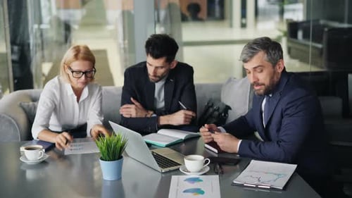 Businesspeople Men and Woman Talking in Cafe Looking at Papers and Laptop