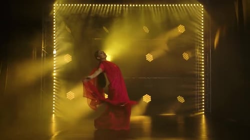 Une jeune fille danseuse dans un sari rouge. Danse folklorique indienne. Tourné dans un studio sombre avec de la fumée et du jaune