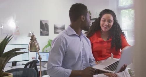 Two happy diverse business people working together, using laptop in modern office