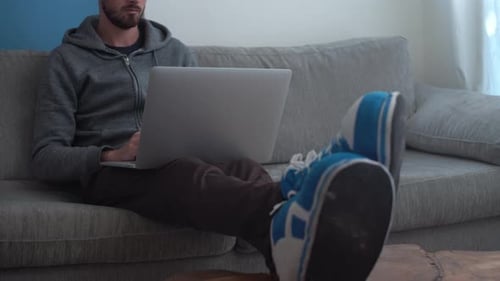 Man sits comfortably on couch and works on laptop from home