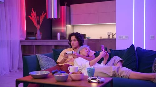 El hombre juega en la consola de juegos con el joystick mientras que la mujer usa un teléfono inteligente con una aplicación de juegos Milenial