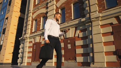 Confident Young Manager with Briefcase Looks at His Watch Walking Near Office Building on Sidewalk
