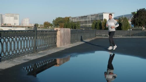 Active Young Man Running Outdoors in City and Enjoying Music Through Headphones in Summer Morning