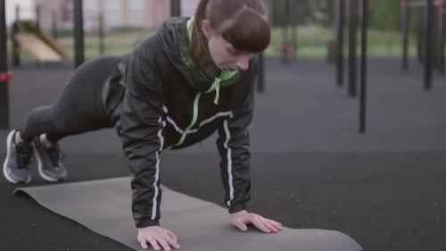 Athletic Woman Does Pushups on a Mat Outdoors