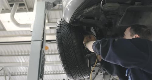 Mechanic Working Underneath Car in Automotive Garage