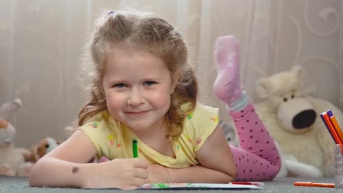 Niña rubia y rizada de cuatro años dibuja con un rotulador en una hoja de papel.