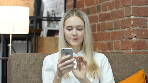 Young Woman Scrolls on Smartphone Device While on Couch