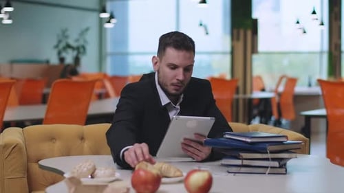 Portrait d'un homme d'affaires caucasien concentré mangeant un croissant sur Internet sur tablette