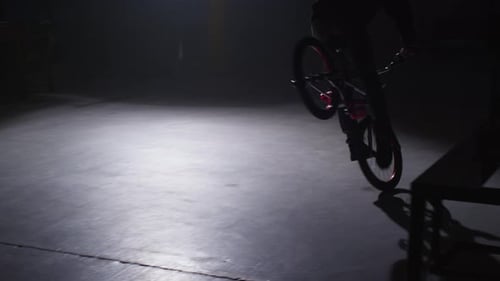 BMX rider doing tricks in dark warehouse.