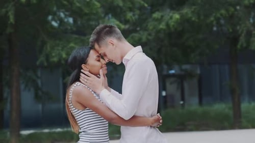 Mixed-race Adults in Love Snuggling By Foreheads To Each Other in Park