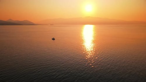 Sunset on the Ionian Sea coast, Greece. Bright Sun, land in the distance, floating boat