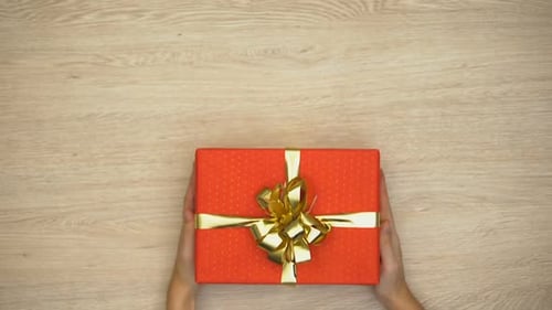 Woman Hands Putting Gift Box on Wooden Background, Holiday Celebration, Top View