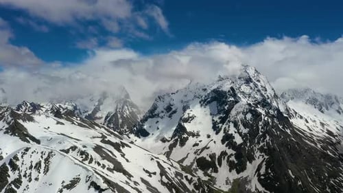 Air Flight Through Mountain Clouds Over Beautiful Snowcapped Peaks of Mountains and Glaciers