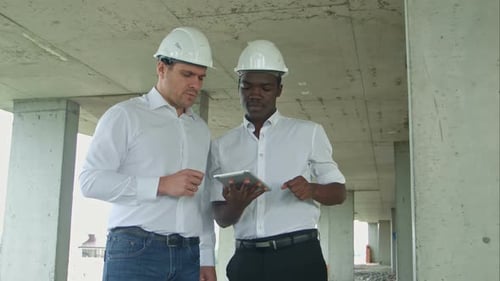 Afroamerikanischer Ingenieur und kaukasischer Architekt nutzt digitales Tablet und trägt Schutzhelme bei