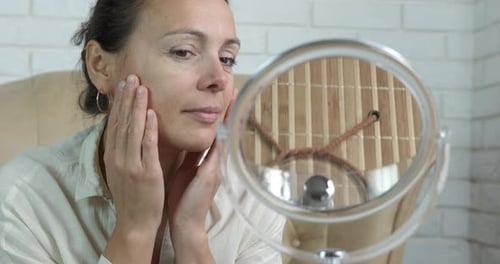 Woman Examines Face in Mirror, Touching Skin