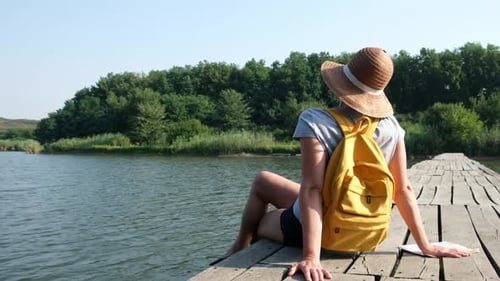 Traveler Hiker with Backpack Sitting on Wooden Bridge Across River in the Forest Resting