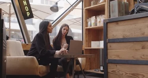 Dos mujeres sentadas y trabajando en un café de estilo moderno e industrial