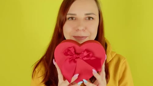 Woman Holding Heart-shaped Gift Box on Yellow Background