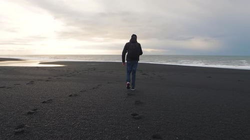 Man Traveler Walking on Volcanic Black Sand Beach in Iceland