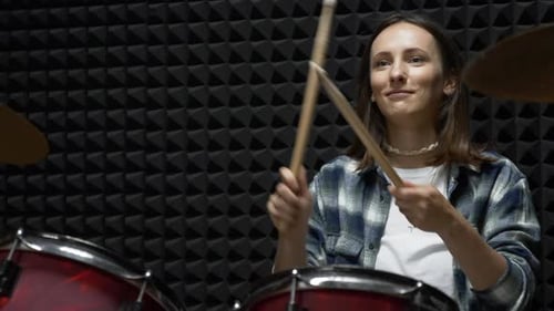 Young stylish woman is playing drums during music band rehearsal in professional vocal studio