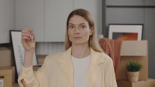 Portrait of Female Owner Holding House Key Looking at Camera Smiling in Light Room