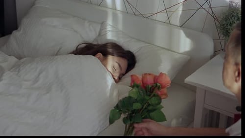Man Gives Roses to Sleeping Woman in Bedroom