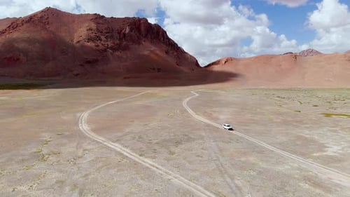 Aerial View of a Car Driving in a Curved Dirt Road in the Tajikistan Desert