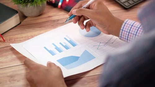 Rear View of Man Hand with Pen Analyzing Bar Chart on Paper